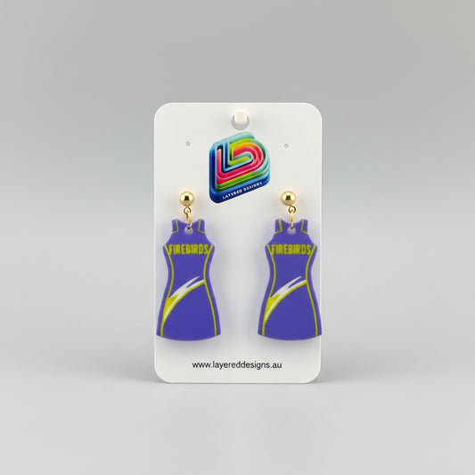Pair of purple dress-shaped earrings on a Layered Designs card with a gray background