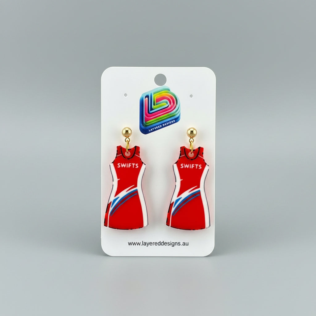 Red dress-shaped earrings on a Layered Designs card against a gray background