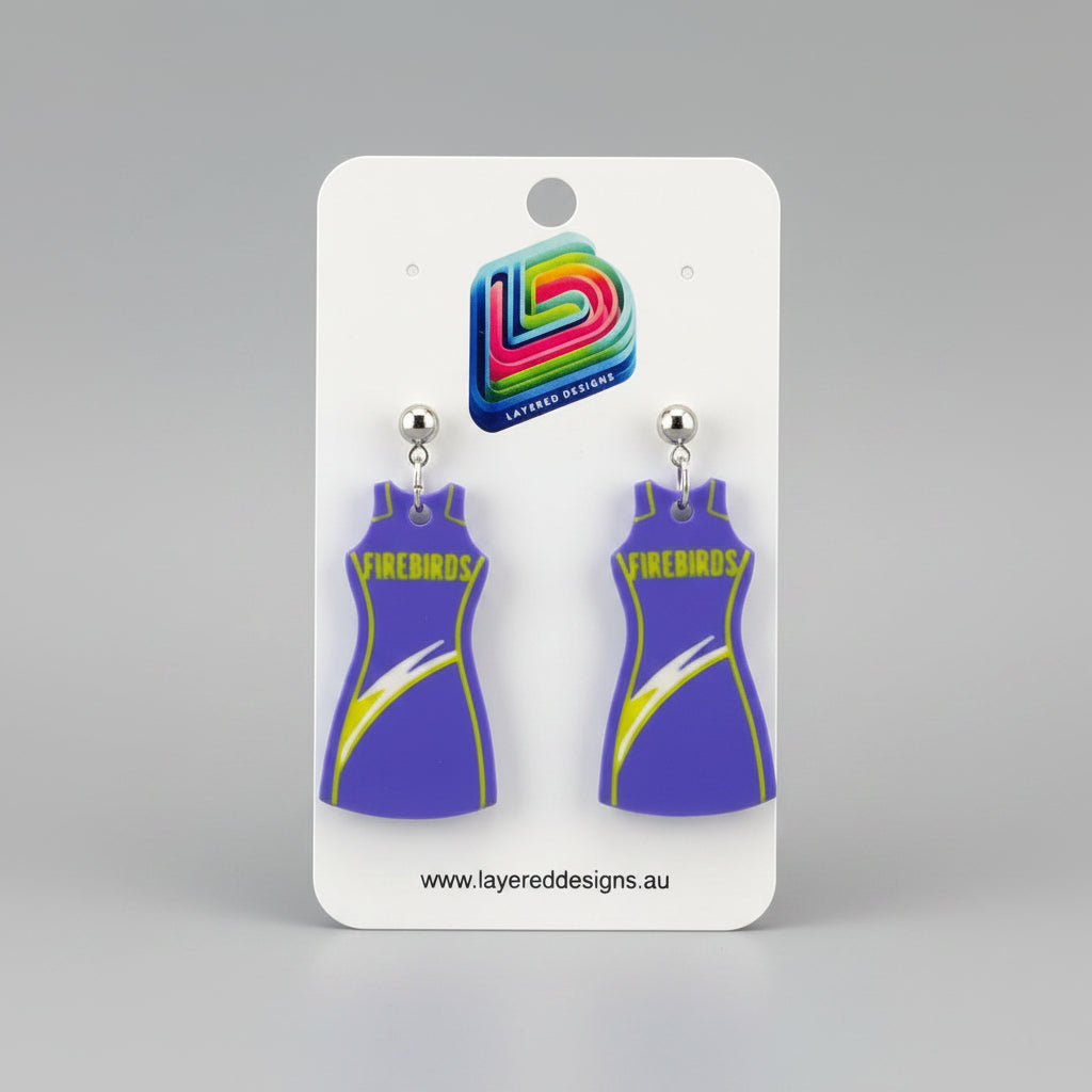 Pair of purple dress-shaped earrings on a Layered Designs card with a gray background