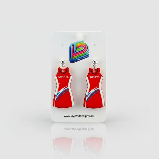 Red dress-shaped earrings on a Layered Designs card against a gray background